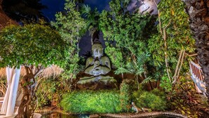 A serene indoor garden with a Buddha statue, lush greenery, and a small pond.