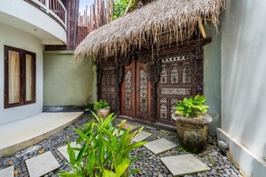 Una verja de madera tradicional con intrincados grabados, una estructura de techo de paja y un camino de piedra que conduce a un edificio.
