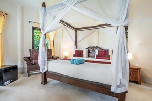 Una cama con dosel de cuatro postes, cortinas blancas, cabecera de madera y almohadas rojas y blancas.