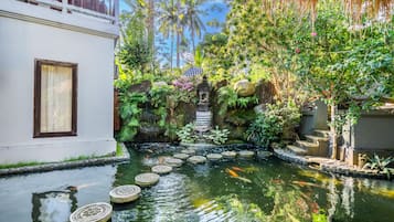 Een rustige tuin met een waterpartij, stenen trappen en weelderige begroeiing.