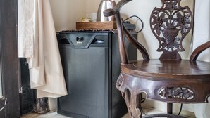 Ein kleiner Küchenbereich mit einem schwarzen Kühlschrank, einem Holzsessel mit aufwendigen Schnitzereien und einem beige gefärbten Vorhang, der zur Seite gezogen ist.