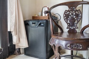Un petit espace cuisine comprenant un réfrigérateur noir, une chaise en bois aux sculptures complexes et un rideau beige partiellement tiré sur le côté.