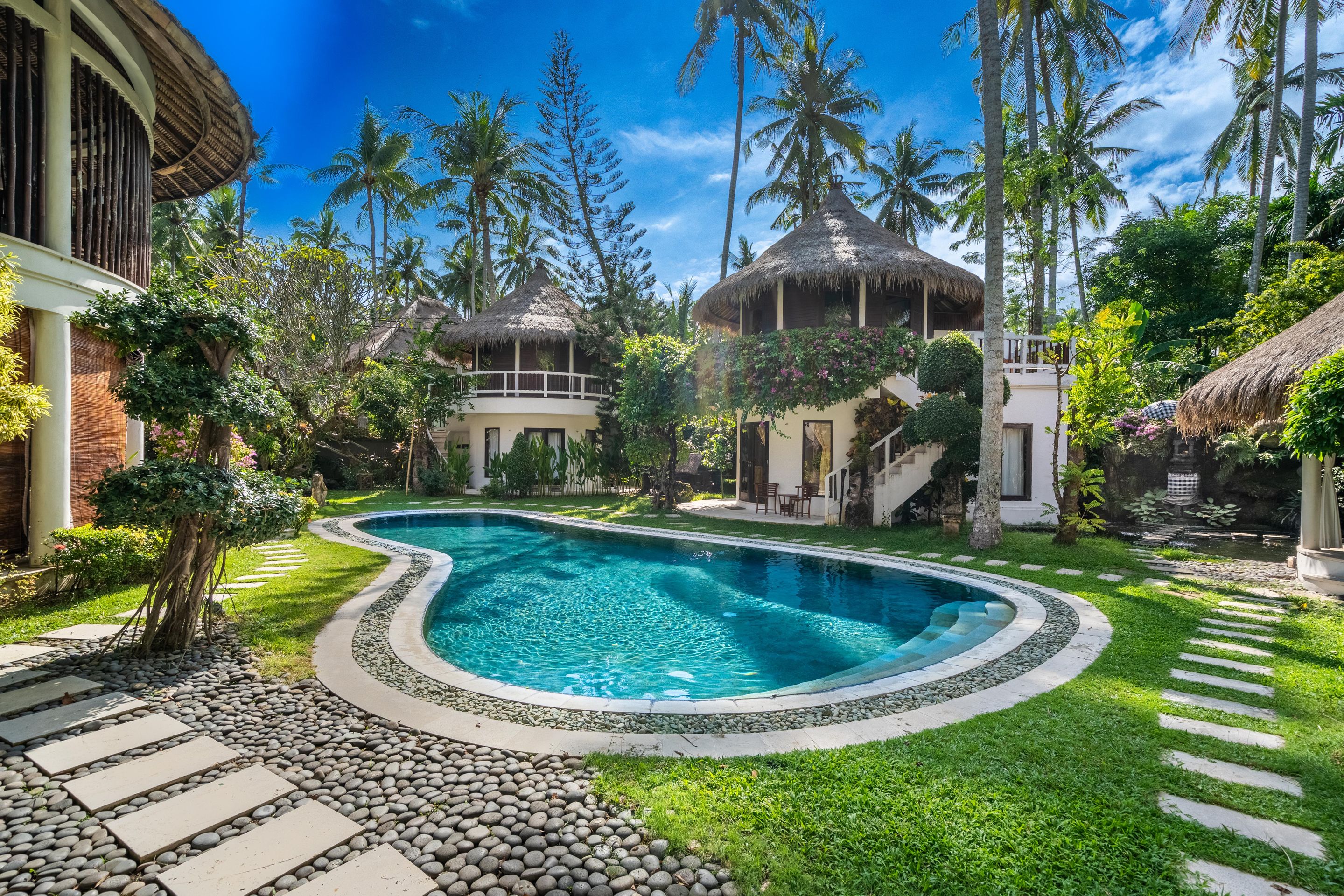 Piscina cercada por vegetação tropical e construções com telhados de palha.
