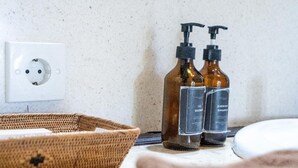 Ein Badezimmer mit einem weißen Waschbecken, zwei braune Flaschen mit den Aufschriften 'gel shower' und 'ever fresh shampoo', einer weißen Steckdose und einem gewobenen Korb.