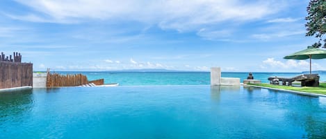 Una piscina azul cristalina con cubierta de madera y vista al océano.