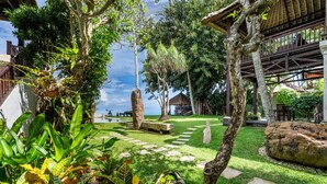 Un jardín tropical con un sendero de piedra, palmeras y una estructura con techo de paja.