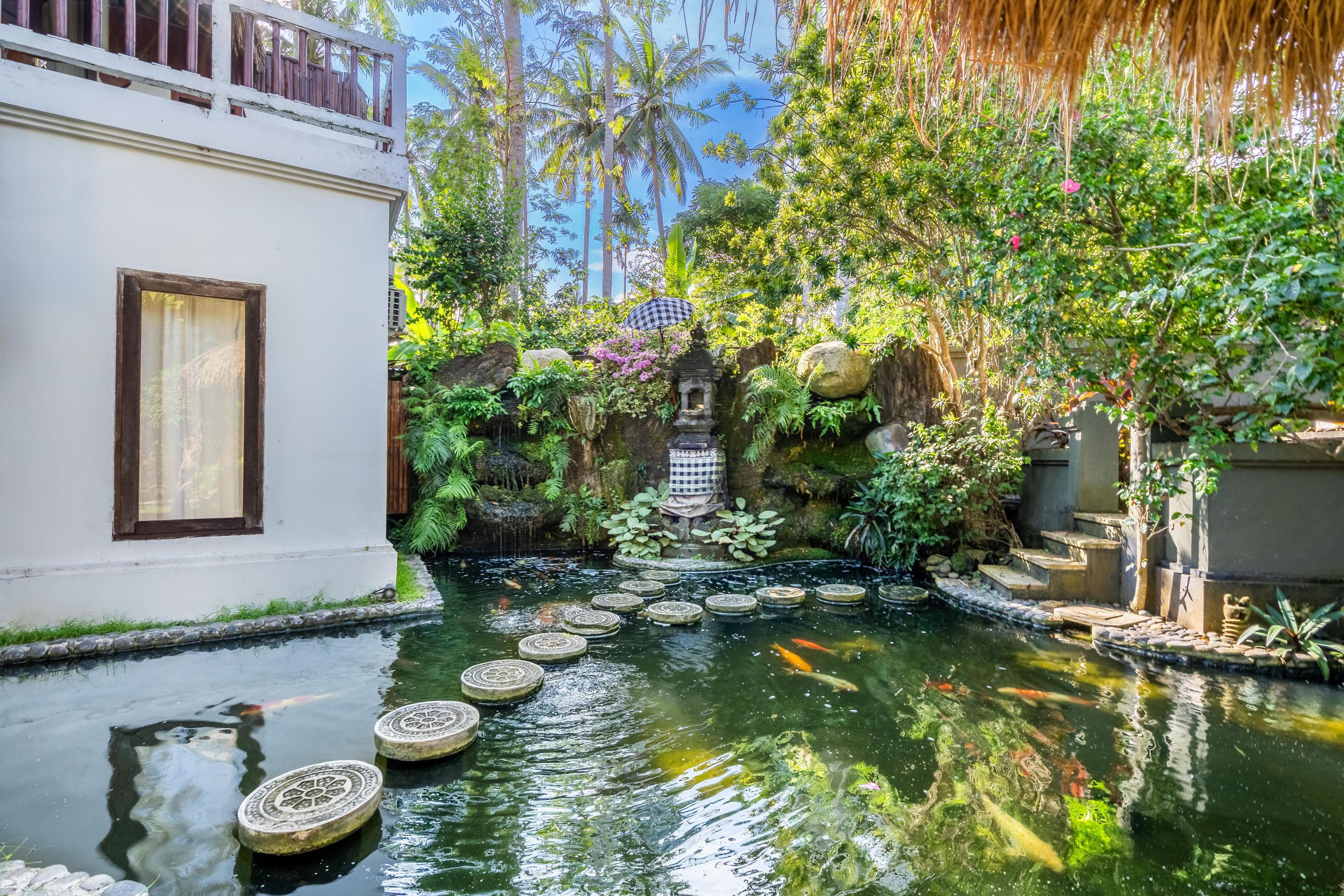 Um jardim tranquilo com um lago ornamental, degraus de pedra e vegetação exuberante.