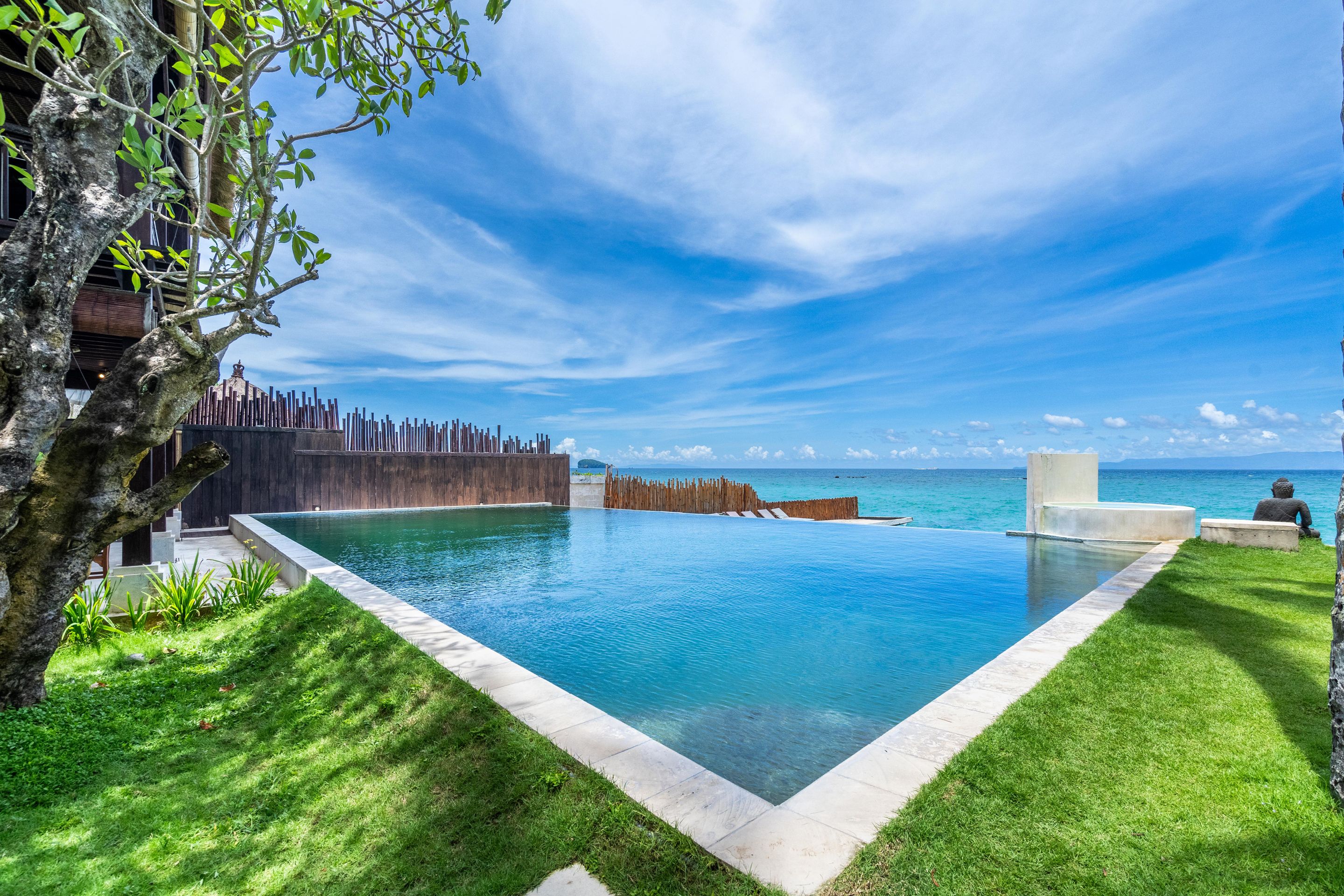 Una piscina a sfioro rettangolare con acqua cristallina blu, circondata da una recinzione in legno e da un prato verde rigoglioso.
