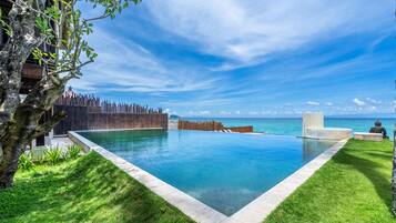 Una piscina a sfioro rettangolare con acqua cristallina blu, circondata da una recinzione in legno e da un prato verde rigoglioso.