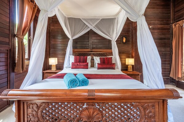 A wooden four-poster bed with a canopy, red and white bedding, and two blue towels. - Double Room with Alley View | The Village of Angels Resort | Candidasa (Kabupaten Karangasem)