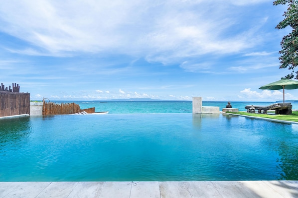 A clear blue pool with a wooden deck and a view of the ocean.