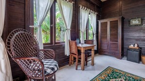 A wooden room with a table and chairs, large windows with curtains, and a traditional rattan chair. - Deluxe Double Room with Balcony and Ocean View | The Village of Angels Resort (Kabupaten Karangasem)