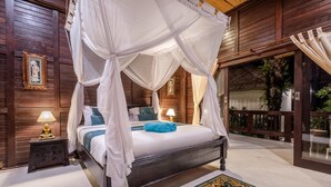A four-poster canopy bed with a blue towel, a nightstand with a lamp, and a patterned rug. - Deluxe Double Room with Balcony and Ocean View | The Village of Angels Resort (Kabupaten Karangasem)