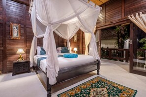 A four-poster canopy bed with a blue towel, a nightstand with a lamp, and a patterned rug. - Deluxe Double Room with Balcony and Ocean View | The Village of Angels Resort (Kabupaten Karangasem)