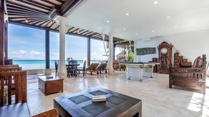 A spacious lounge area with a view of the ocean, wooden furniture, and a pool table.