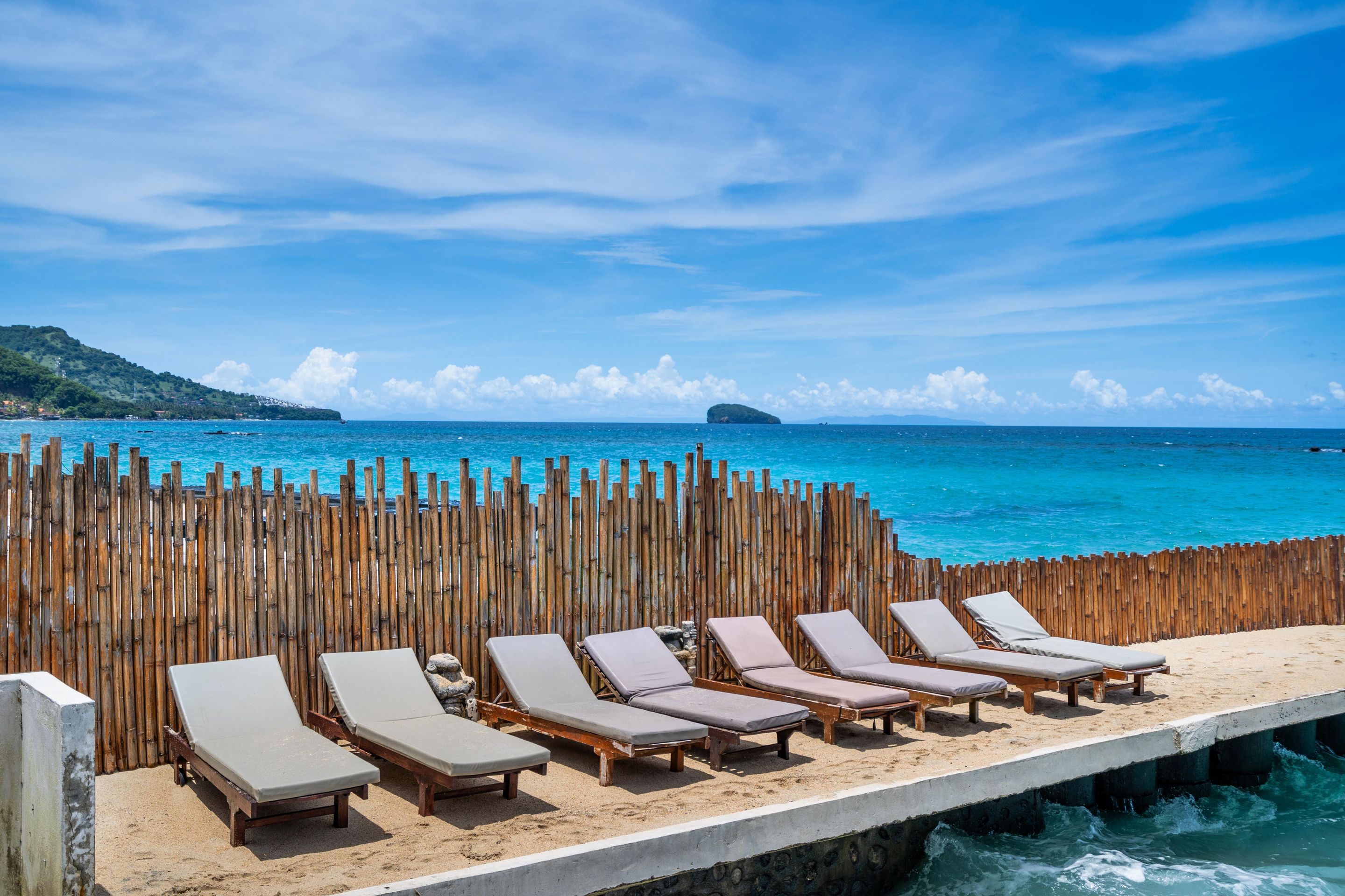 A beachside view with wooden fences, multiple sun loungers, and a clear blue sea.