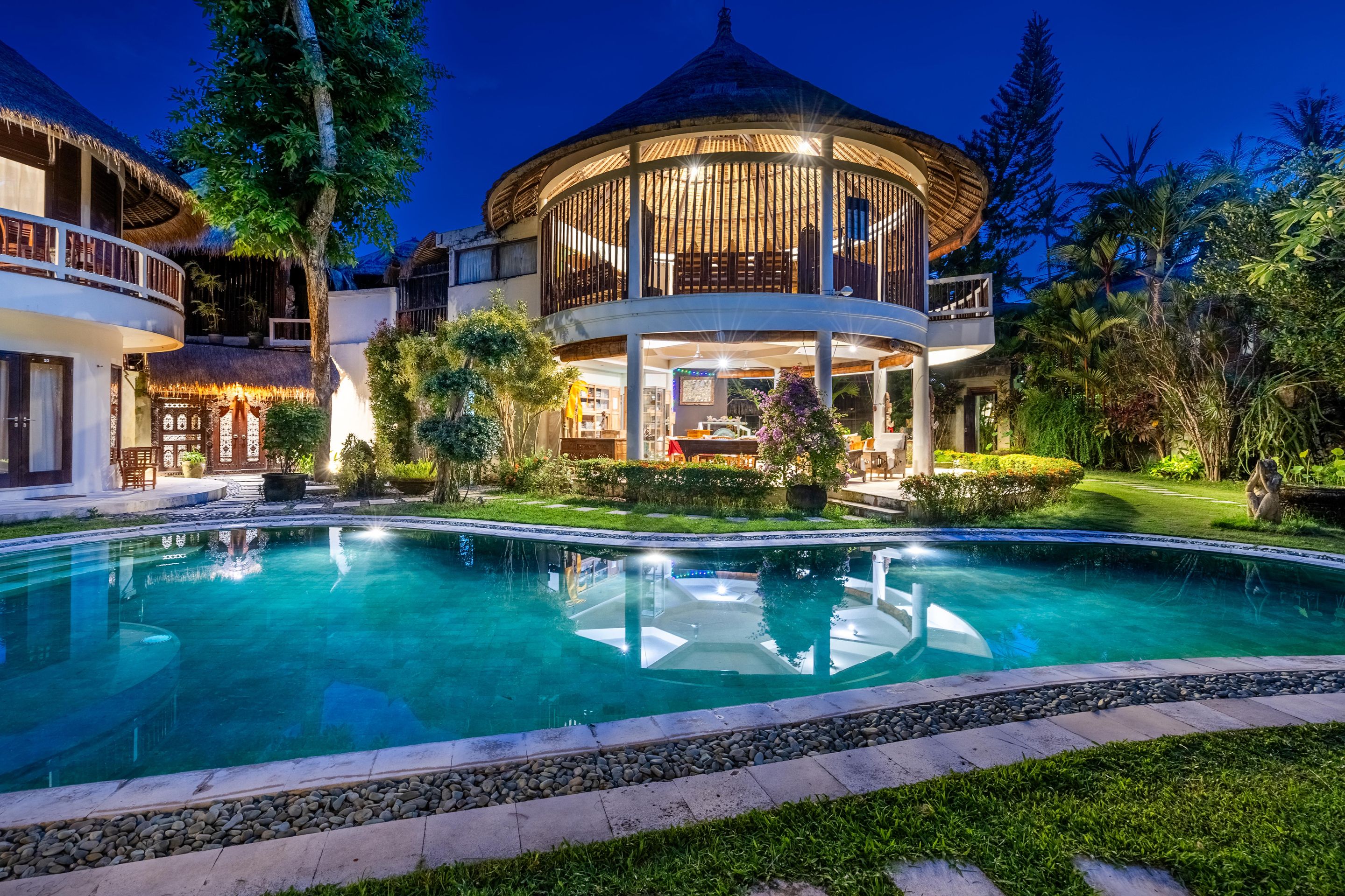 Un resort con una amplia piscina, un espacio al aire libre cubierto y abundante vegetación.