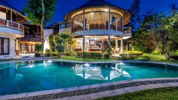Un resort con una amplia piscina, un espacio al aire libre cubierto y abundante vegetación.