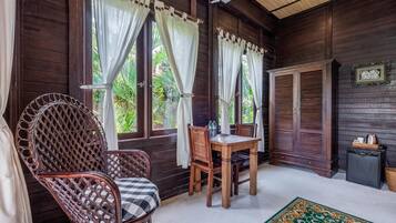 Una habitación de madera con una mesa y sillas, ventanas amplias con cortinas y una silla de ratán tradicional.