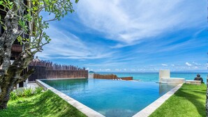 Ein moderner Infinity-Pool mit freiem Blick auf den Ozean, umgeben von gepflegtem Rasen und einem Holenzaun.