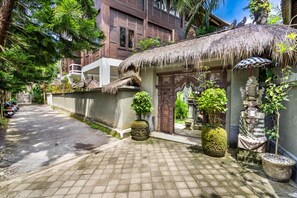 A traditional thatched-roof structure with a stone door, surrounded by potted plants and a paved pathway.