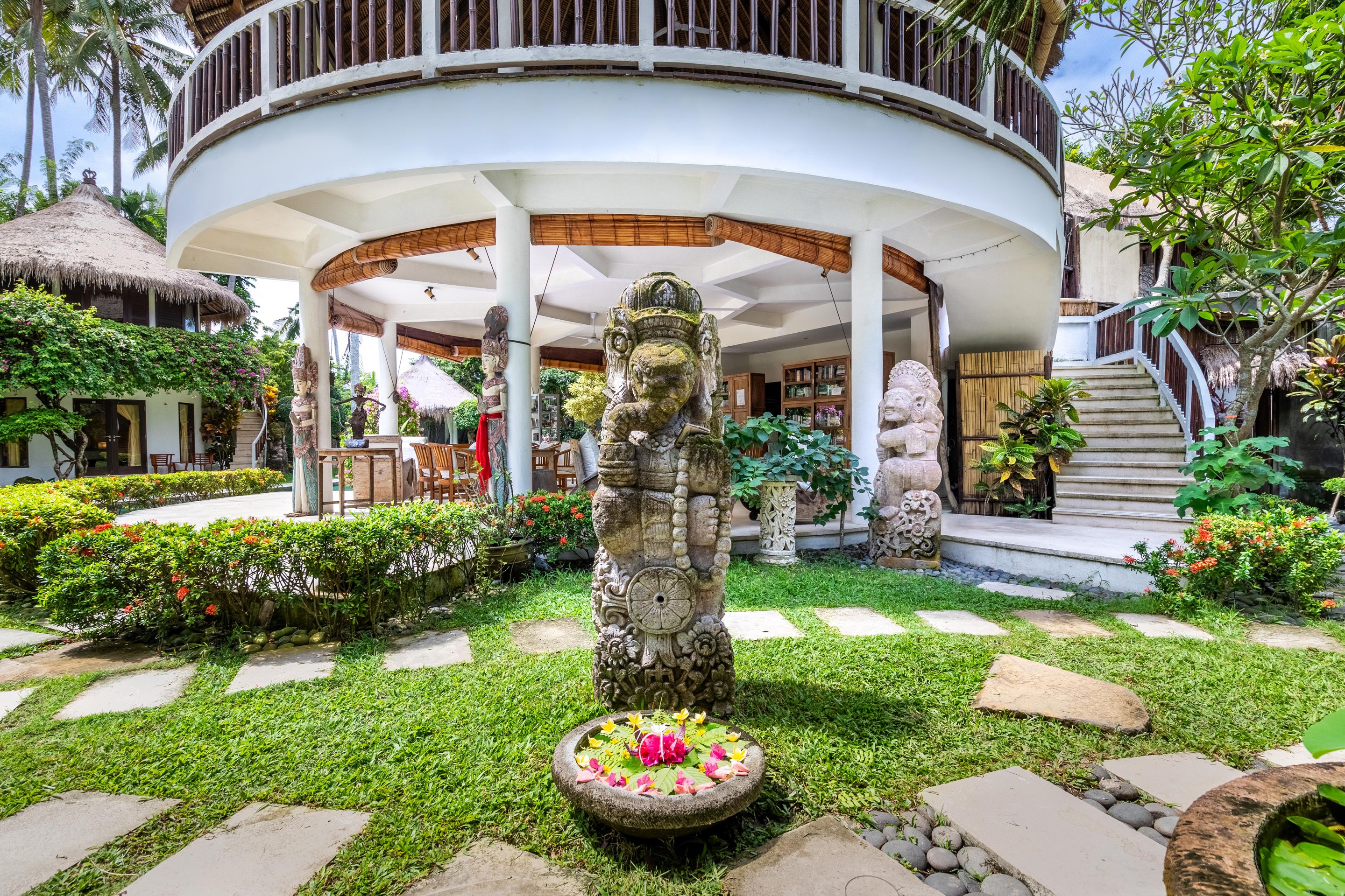 A tropical resort with a circular building, stone statues, and a garden with a water feature.