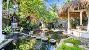A tranquil garden with a pond, stone steps, and a thatched-roof structure.