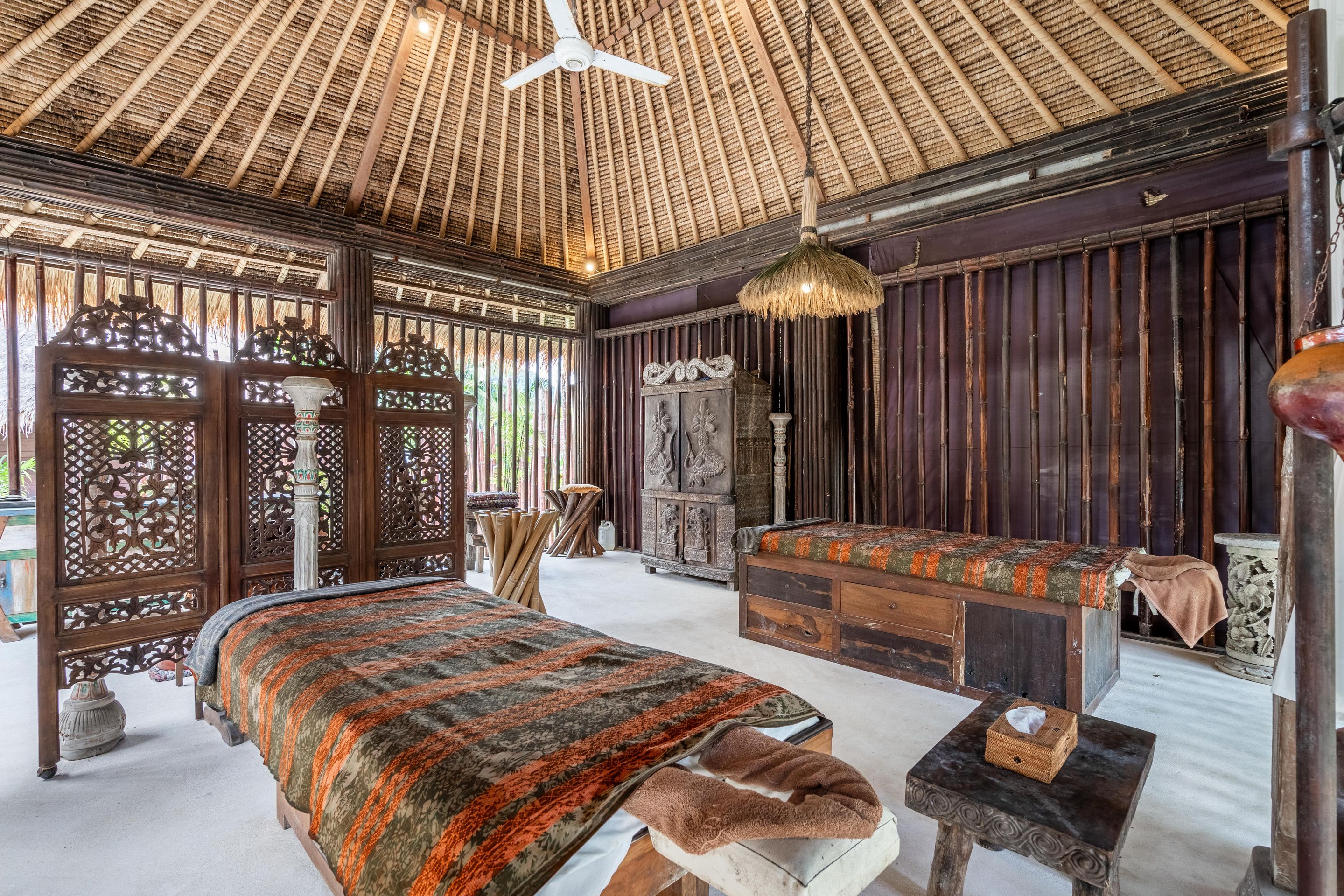 A traditional room with a thatched roof, wooden furniture, and a bed with a patterned bedspread.