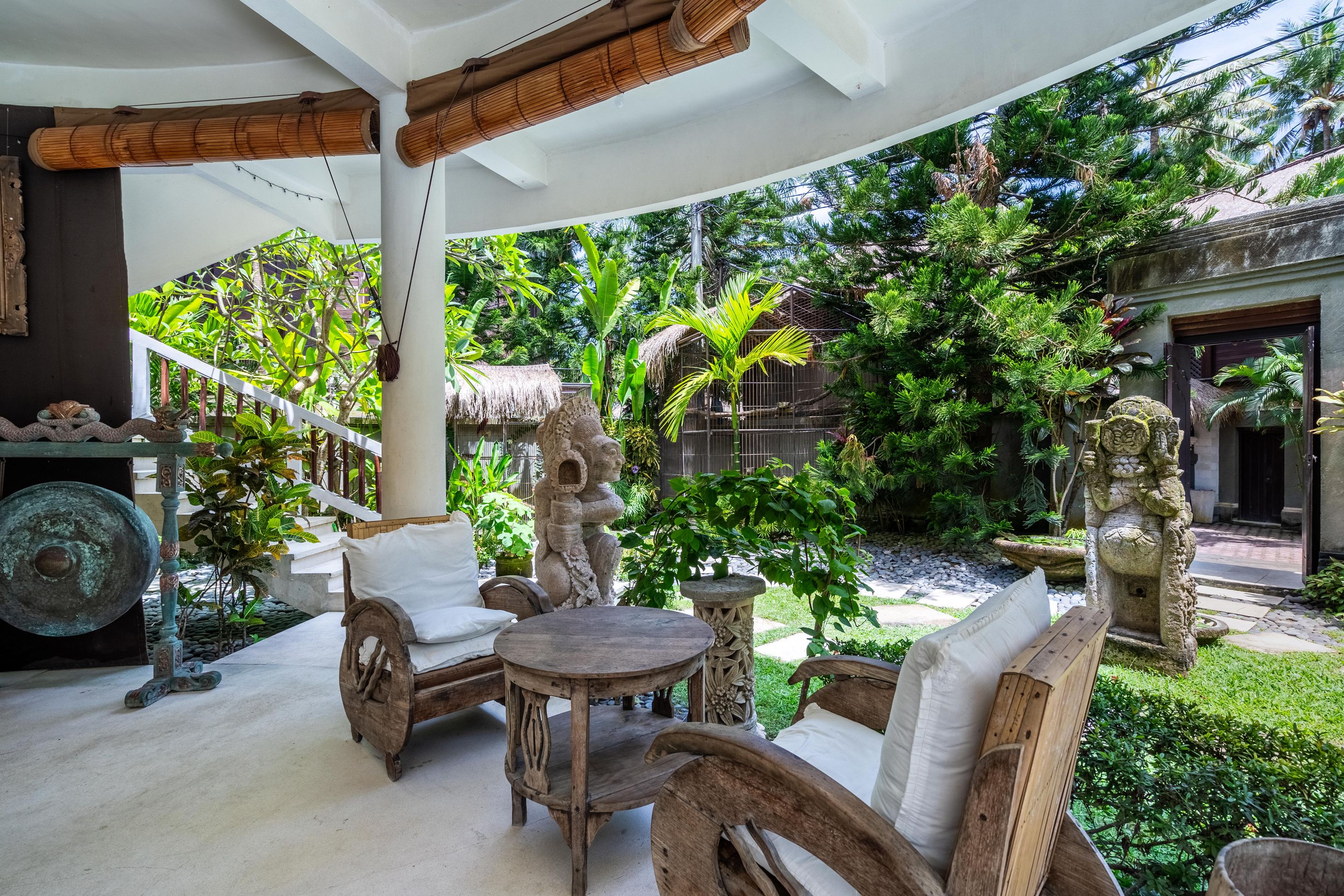 An outdoor seating area with wooden furniture, a stone statue, and lush greenery.