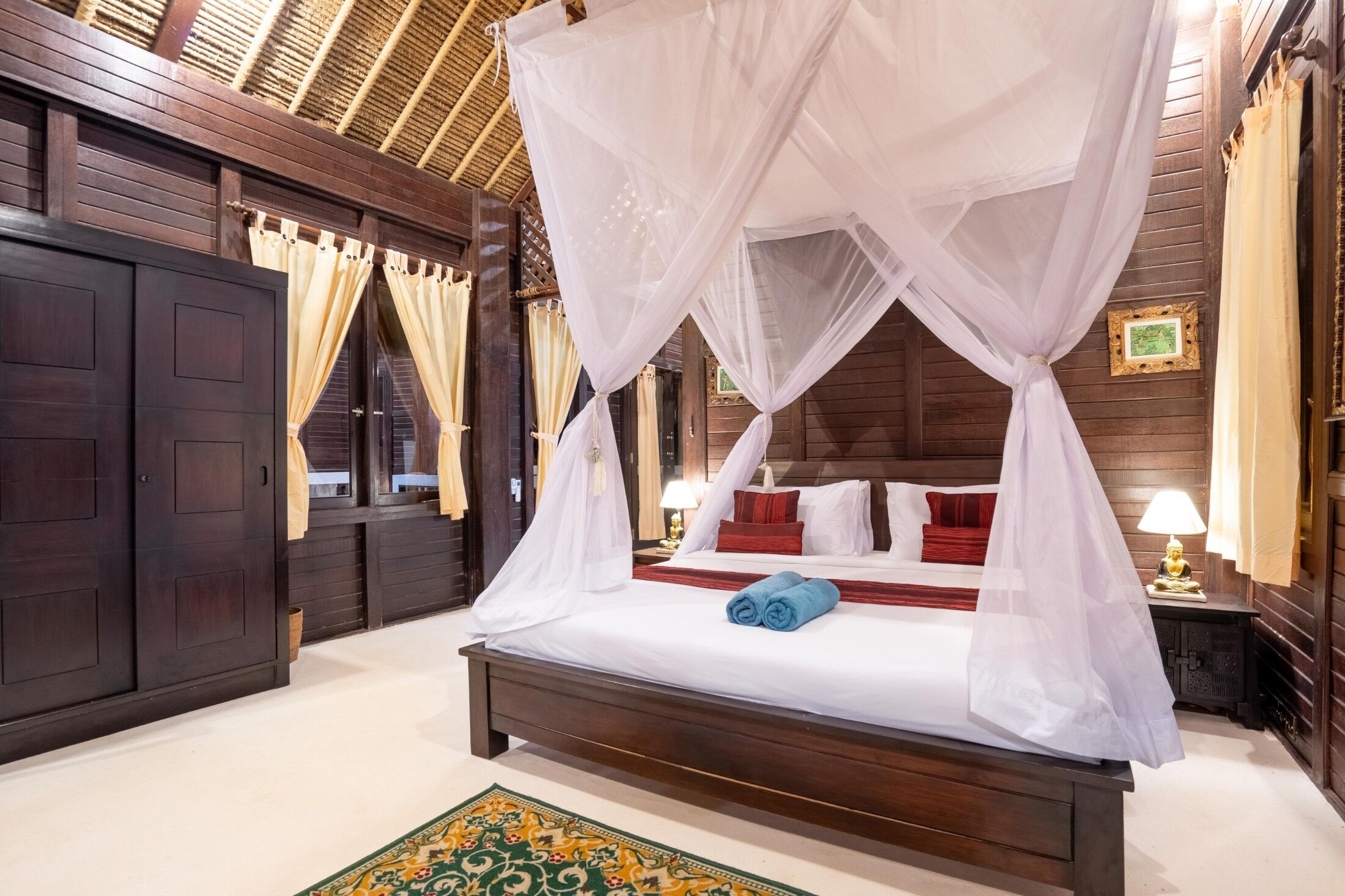 A four-poster canopy bed with white linens, red pillows, and a blue towel.