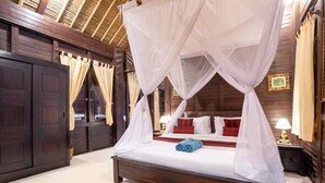 Een hemelbed met witte lakens, rode kussens en een blauwe handdoek.