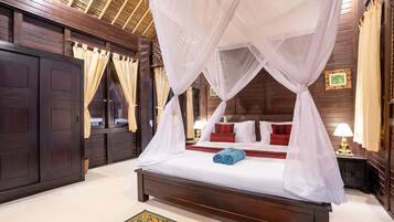 A four-poster canopy bed with white linens, red pillows, and a blue towel.