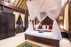A four-poster canopy bed with white linens, red pillows, and a blue towel.