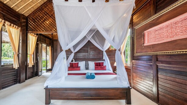 Een bed met hemelbed, houten wanden en een kamerbreed tapijt met patroon.