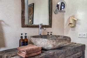 A bathroom with a large stone sink, a wooden vanity, a mirror, and two bottles of shampoo.