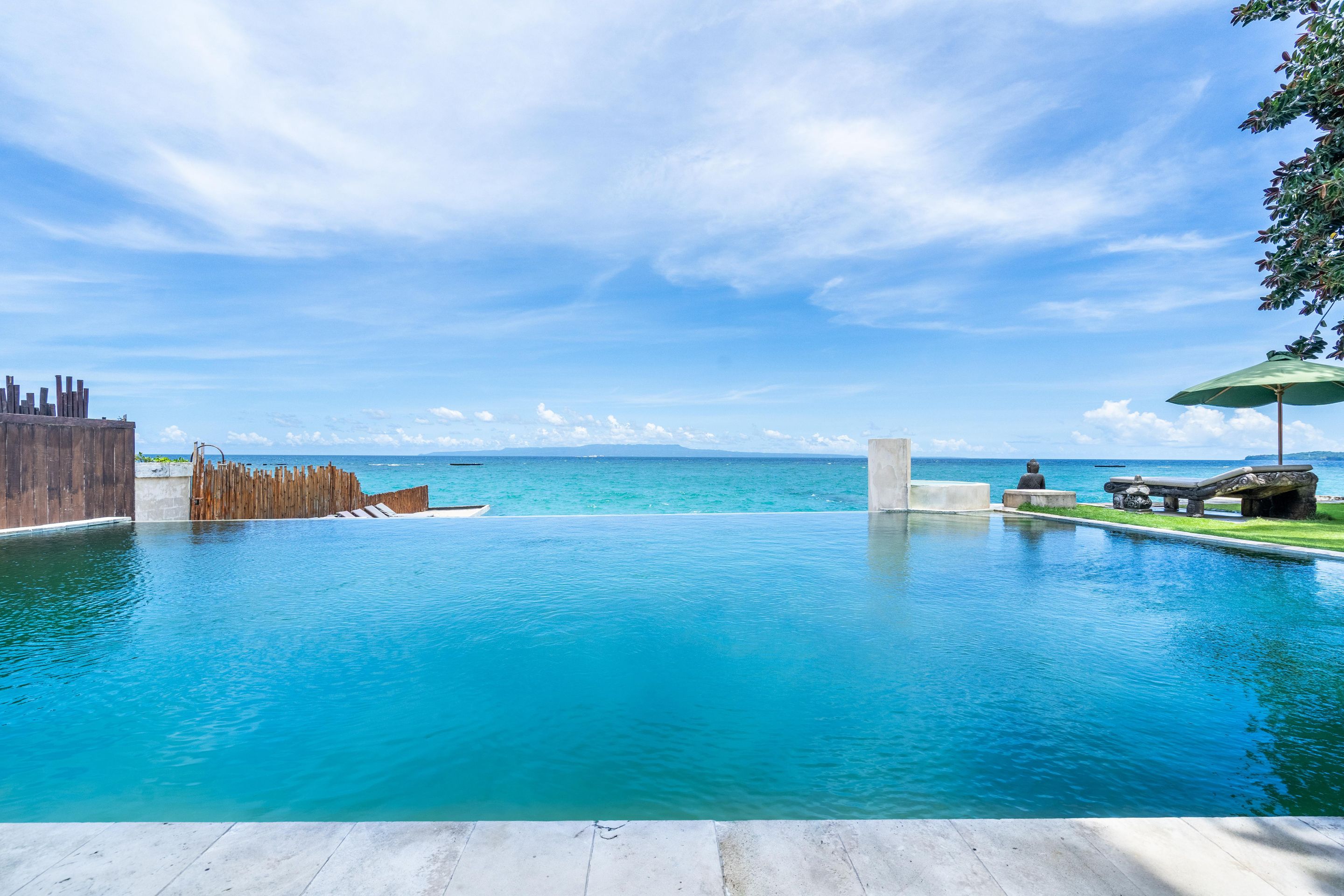 A clear blue pool with a wooden deck and a view of the ocean.