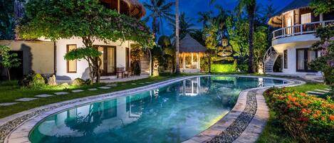 A resort with a swimming pool, thatched-roof structures, and lush greenery.