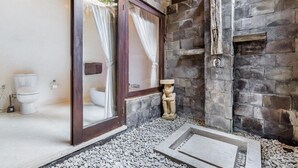 Un baño con pared de piedra, una estatua de piedra y una puerta de cristal que da al inodoro.