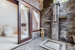 Een badkamer met een stenen muur, een stenen beeld en een glazen deur naar een toilet.