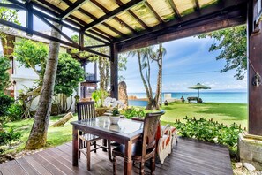 A wooden deck with a glass table and chairs overlooking a beach. - Superior Oceanview Group Stay – 2 Levels, Separate Entrances | The Village of Angels Resort (Kabupaten Karangasem)