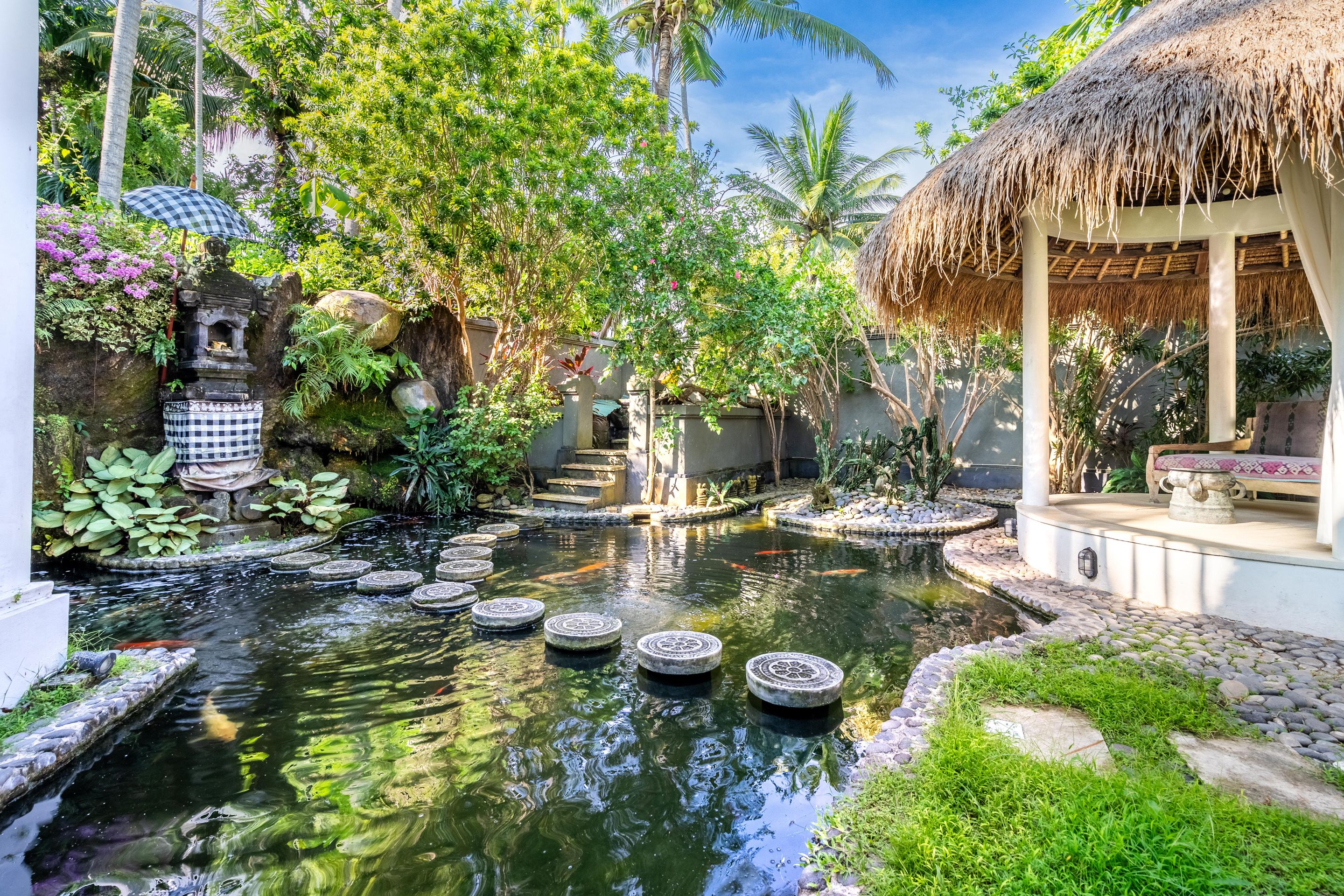 A tranquil garden with a pond, stone steps, and a thatched-roof structure.