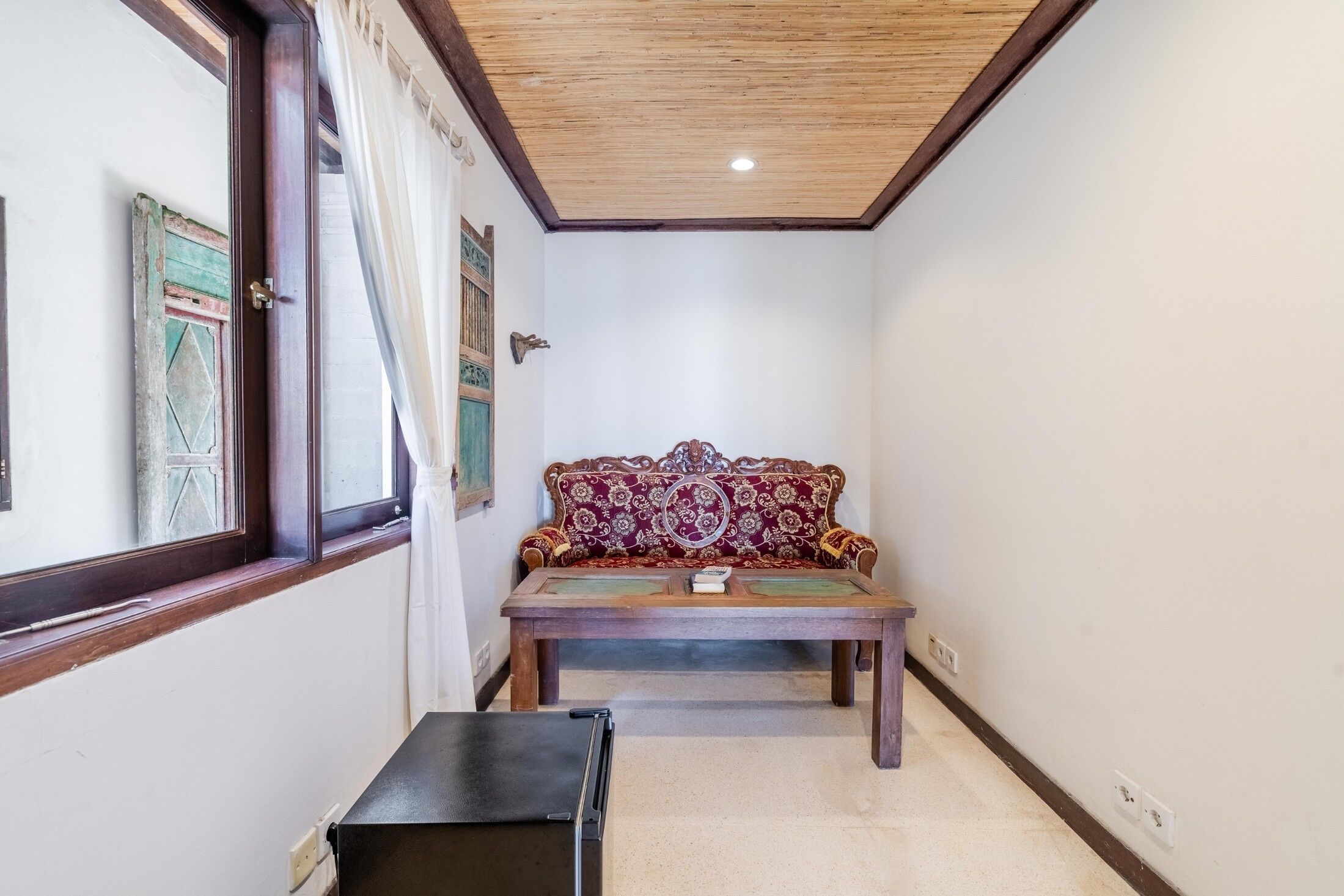 Un estrecho pasillo con un banco de madera, una puerta con un tirador decorativo y una ventana con cortinas.