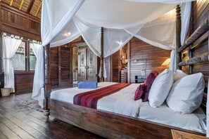Een houten hemelbed met witte lakens en een rode en zwarte plaid.