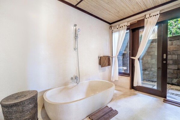 A bathroom with a freestanding bathtub, a showerhead, a towel rack, and a stone wall.
