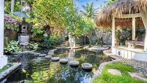 A serene garden with a pond, stone stepping stones, a thatched-roof structure, and lush greenery. - Oceanview Stay – 2 Levels, Separate Entrances | The Village of Angels Resort (Kabupaten Karangasem)