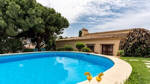 A swimming pool with a clear blue water surface, surrounded by a well-maintained lawn and a building with a tiled roof.