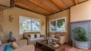 A cozy room with wicker furniture, a wooden ceiling, and a view of palm trees.