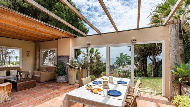 A patio area with a table set for dining, outdoor furniture, and a view of the sea.