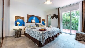 A bedroom with a bed, bedside lamps, a ceiling fan, a large window with a view, and a patterned rug.
