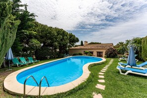 Una piscina de borde curvo, rodeada de un césped cuidado y un edificio con tejado de baldosas al fondo.